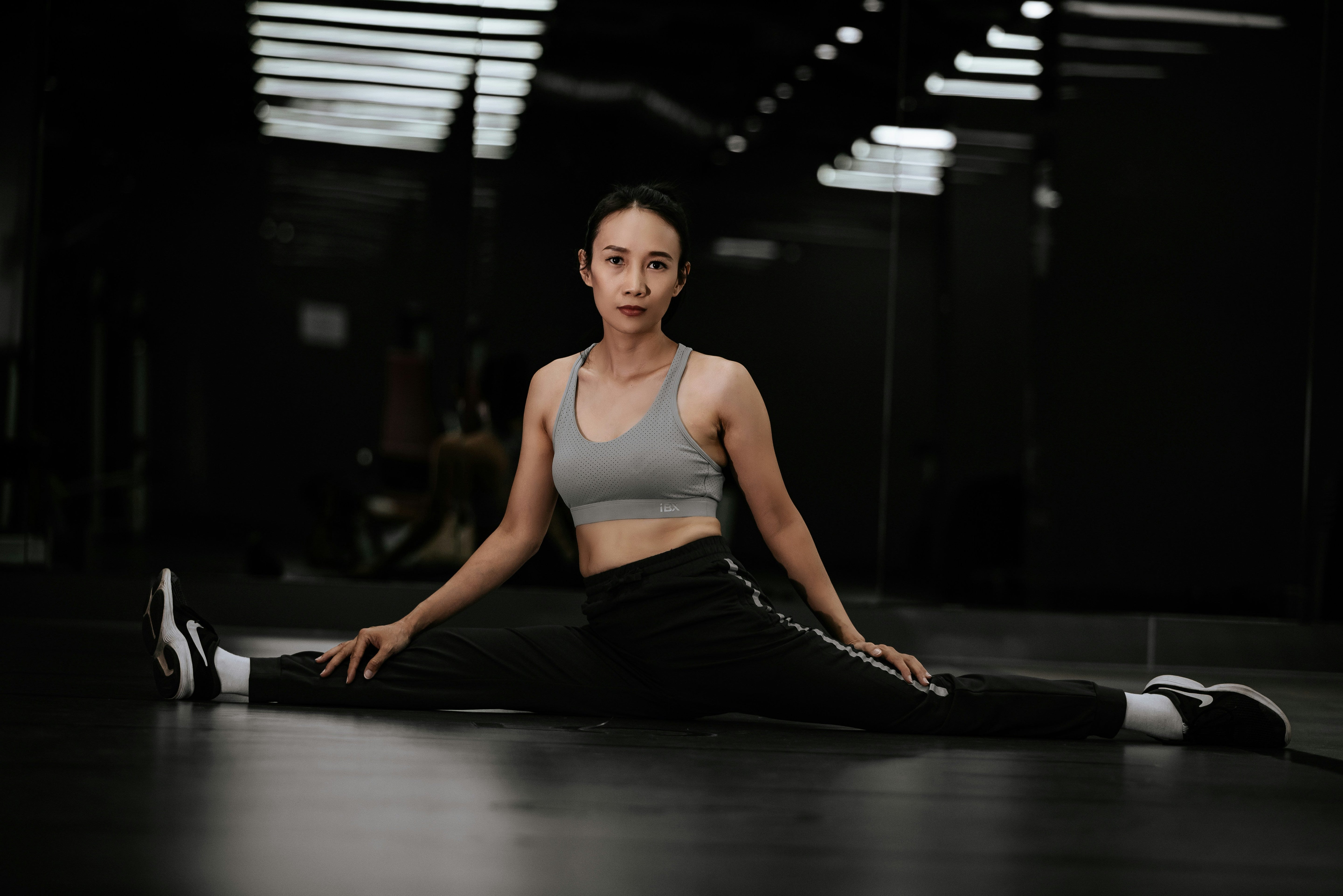 A lady in gymwear doing the splits in a dark gym