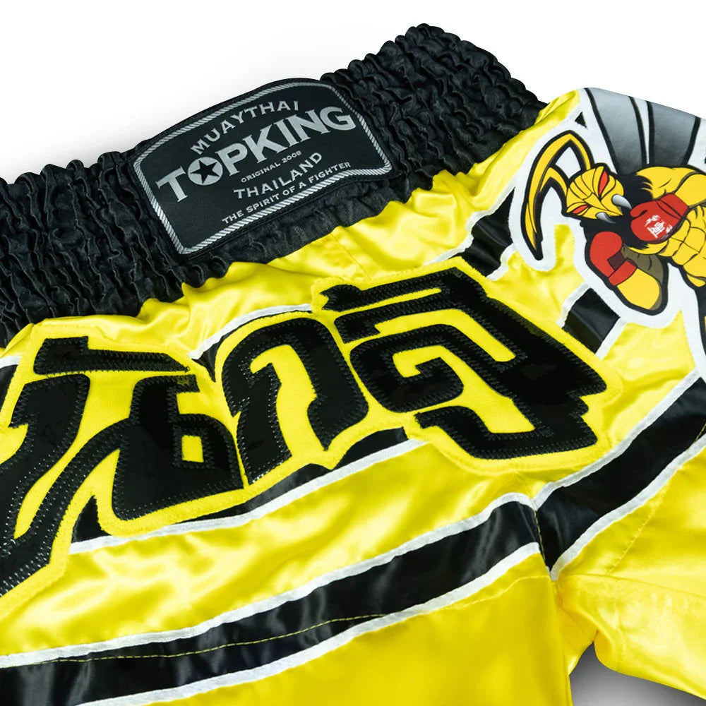 Top King Muay Thai yellow shorts with black waistband, Thai script, and killer bee graphic.